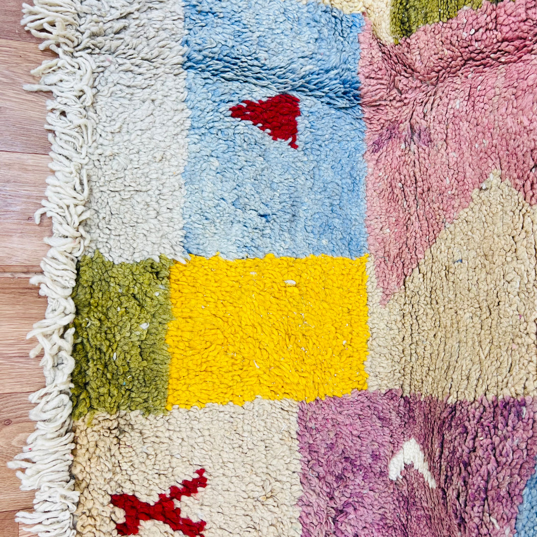 Vintage Moroccan wool rug with colorful patchwork design in pink, yellow, blue, and olive. Handwoven by artisans in the Atlas Mountains.