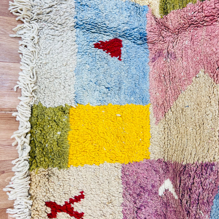 Vintage Moroccan wool rug with colorful patchwork design in pink, yellow, blue, and olive. Handwoven by artisans in the Atlas Mountains.
