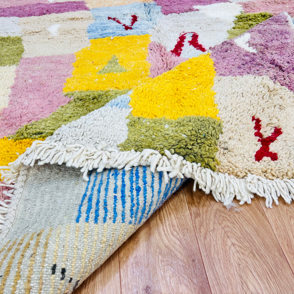 Vintage Moroccan wool rug with colorful patchwork design, showcasing pinks, yellows, blues, and greens. Handwoven by Berber artisans.