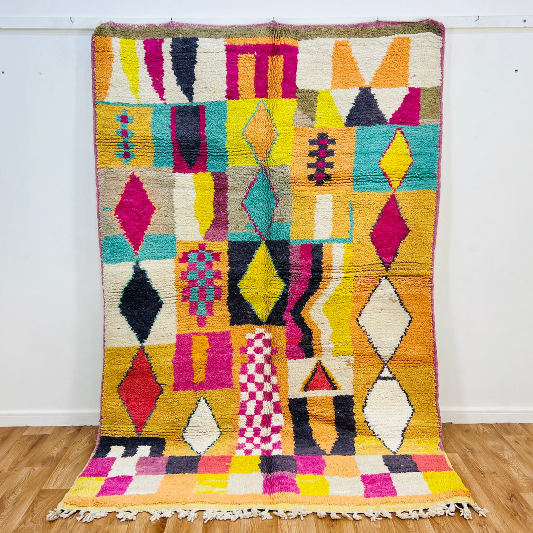 Colorful Beni Mrirt Moroccan rug with diamond and checkerboard motifs in pink, yellow, black, and teal. Handmade wool carpet.