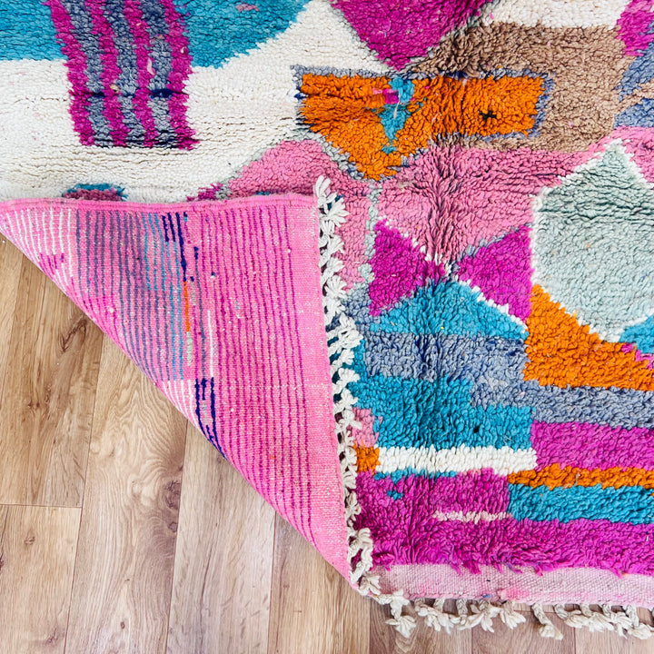 Colorful Moroccan wool rug with geometric patterns in pink, orange, turquoise, and cream, handmade by Berber artisans.