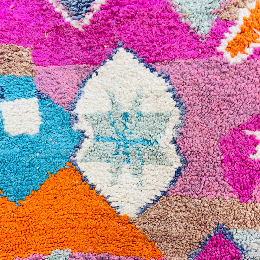 Colorful Moroccan wool rug featuring a vibrant mix of fuchsia, orange, turquoise, and cream geometric patterns.