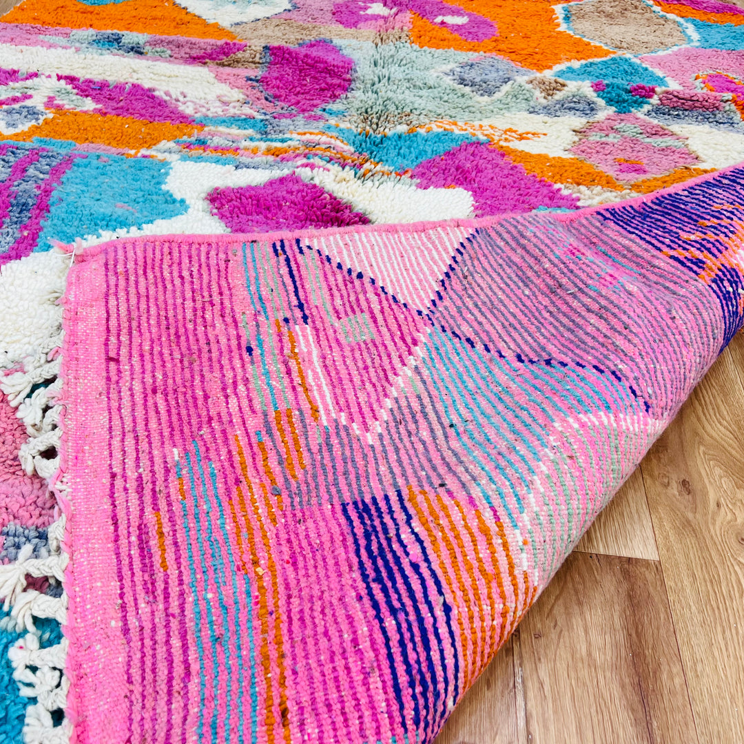 Colorful Moroccan wool rug with vibrant geometric patterns in fuchsia, orange, turquoise, and lavender.
