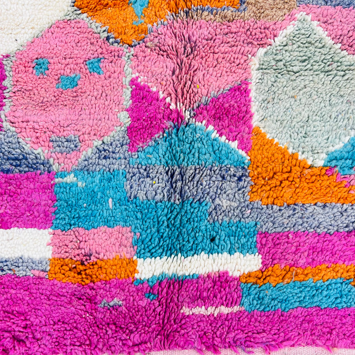 Colorful Moroccan wool rug with geometric shapes in pink, orange, turquoise, and lavender. Handmade by Berber artisans.
