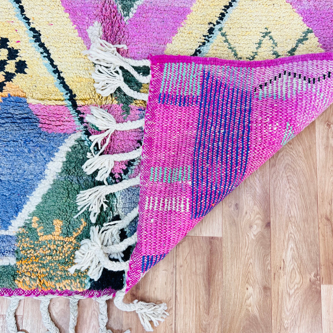 Pink Diamond Moroccan Wool Rug with vibrant colors on wooden floor, showcasing traditional Berber weaving and tassels.