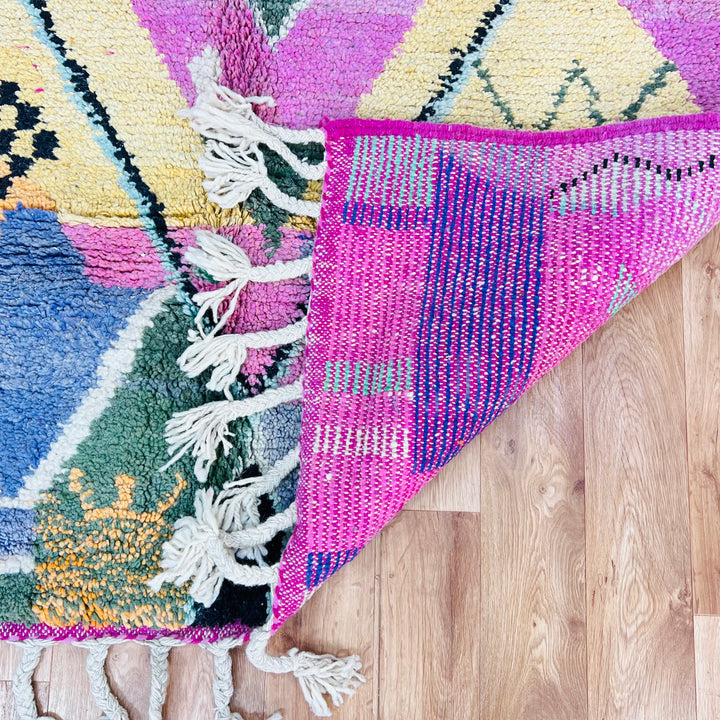 Pink Diamond Moroccan Wool Rug with vibrant colors on wooden floor, showcasing traditional Berber weaving and tassels.