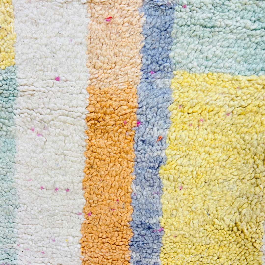 Close-up of a colorful modern abstract Moroccan wool rug showcasing vertical stripes in soft pink, yellow, mint green, and blue.