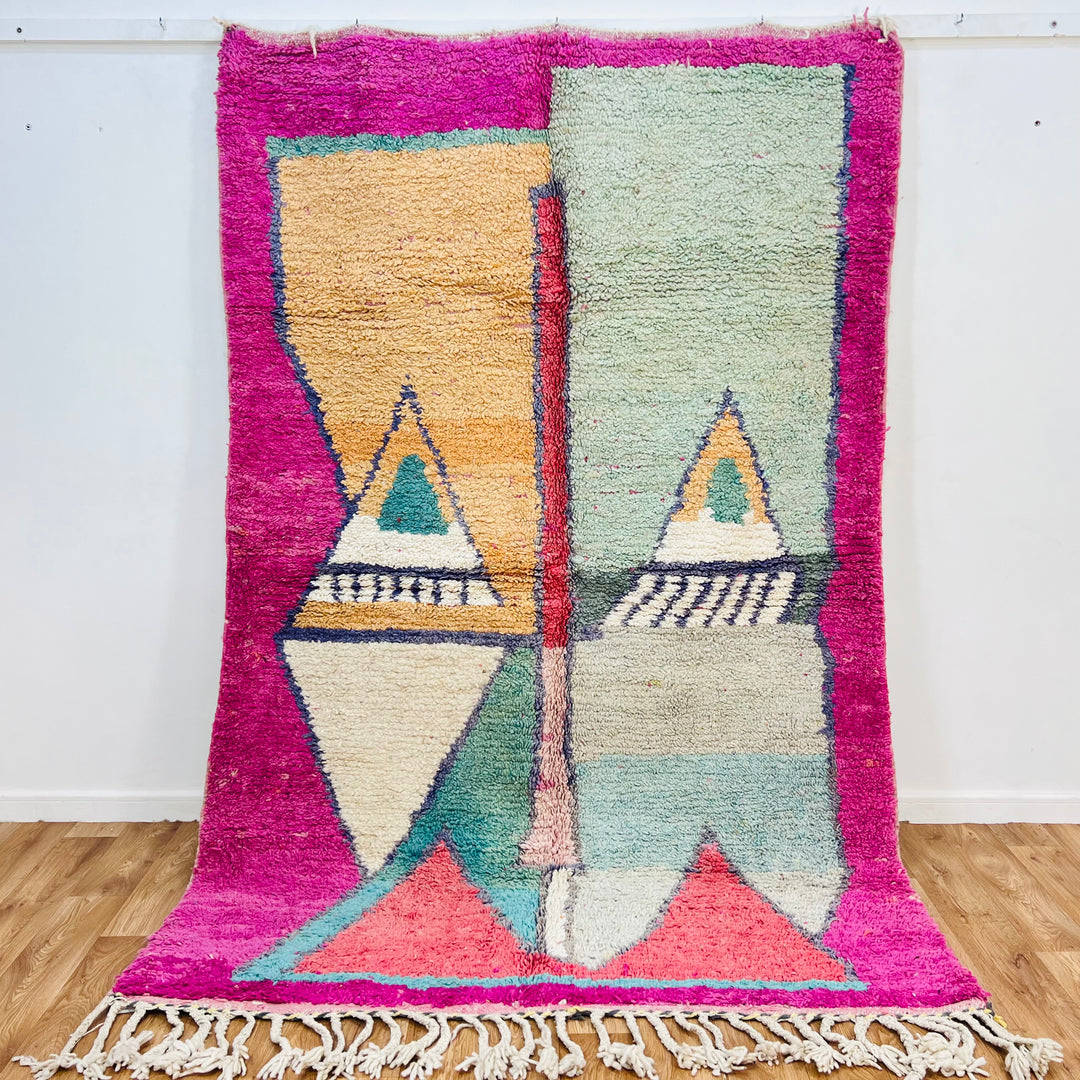 Geometric Moroccan wool rug with mirrored pyramids in peach and mint, fuchsia border, handwoven by Berber artisans; 256 x 168 cm.