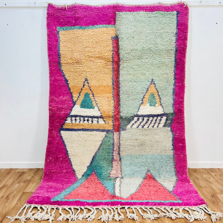 Geometric Moroccan wool rug with pyramid design in peach, mint, navy on fuchsia border. Traditional Berber handwoven style.