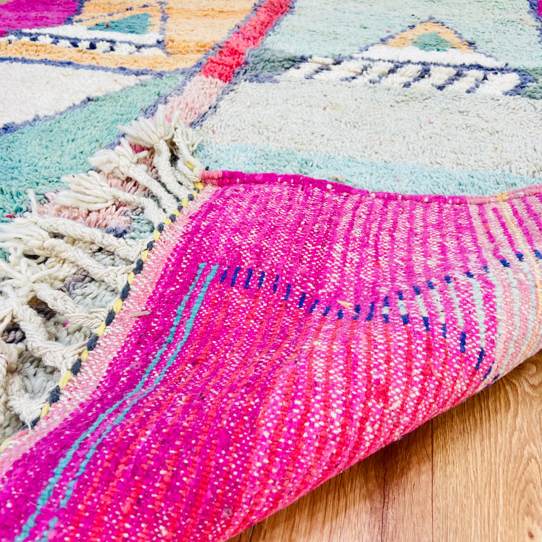 Geometric Moroccan wool rug with pink, mint, and navy patterns, highlighting vibrant Berber craftsmanship on hardwood floor.