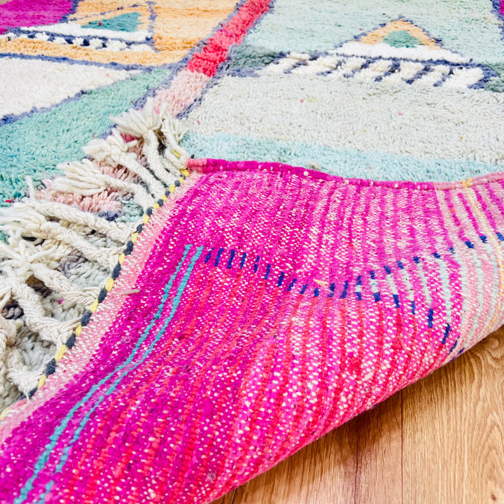 Geometric Moroccan wool rug with pink, mint, and navy patterns, highlighting vibrant Berber craftsmanship on hardwood floor.