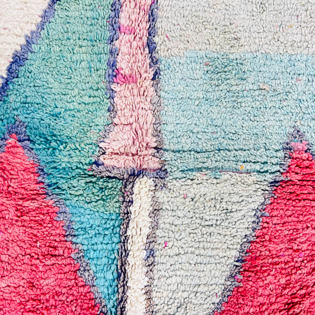 Close-up of a geometric Moroccan wool rug with pink, green, and navy accents. Handwoven traditional Moroccan carpet.