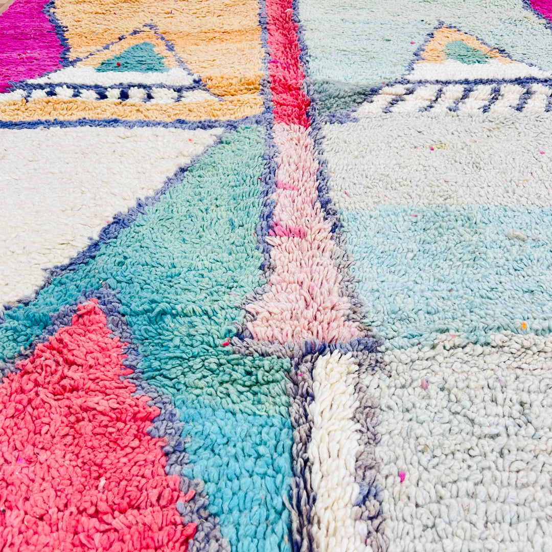 Geometric Moroccan wool rug with mirrored pyramid patterns in peach and mint, navy and white accents, and a vibrant fuchsia border.