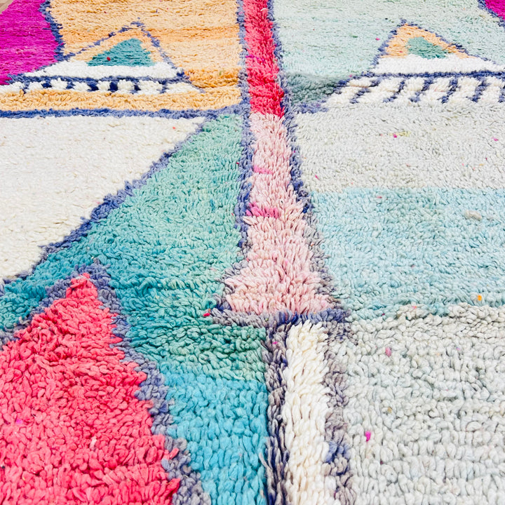 Geometric Moroccan wool rug with mirrored pyramid patterns in peach and mint, navy and white accents, and a vibrant fuchsia border.