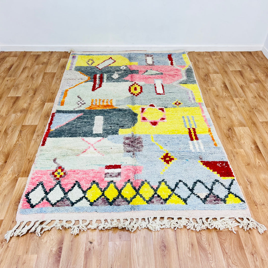 Abstract Berber Moroccan wool rug with geometric shapes and vibrant colors on a wooden floor.