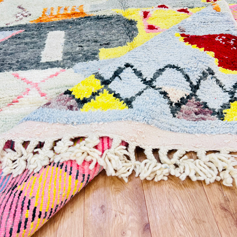 Close-up of Abstract Berber Moroccan Wool Rug with geometric patterns in vibrant colors on wooden floor.