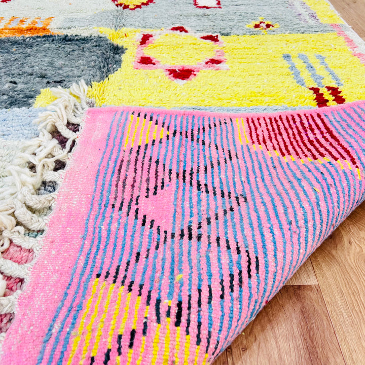 Colorful Moroccan wool rug featuring vibrant geometric patterns, handwoven by artisans with yellow, pink, and grey accents.