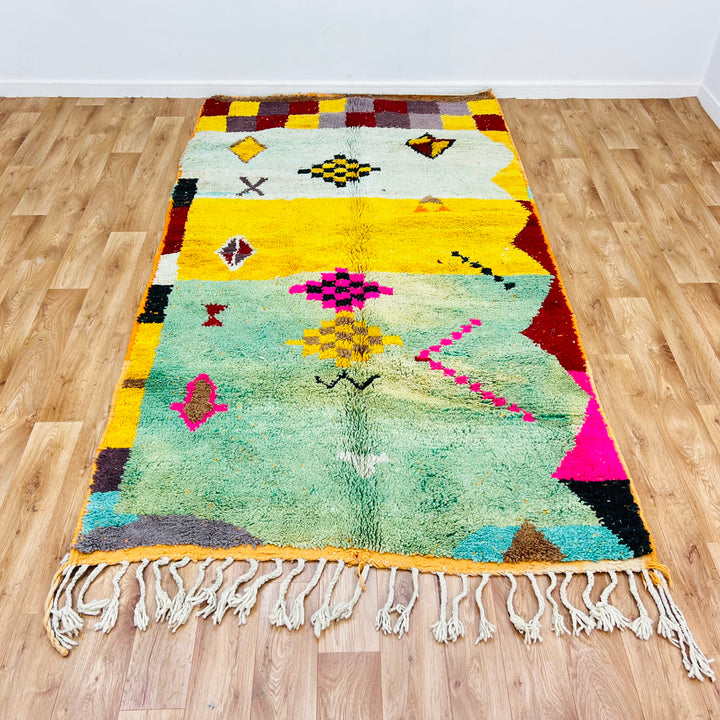 Colorful Moroccan Berber wool rug with tribal symbols on wooden floor, 268 x 150 cm, vibrant decor, handmade in Morocco.