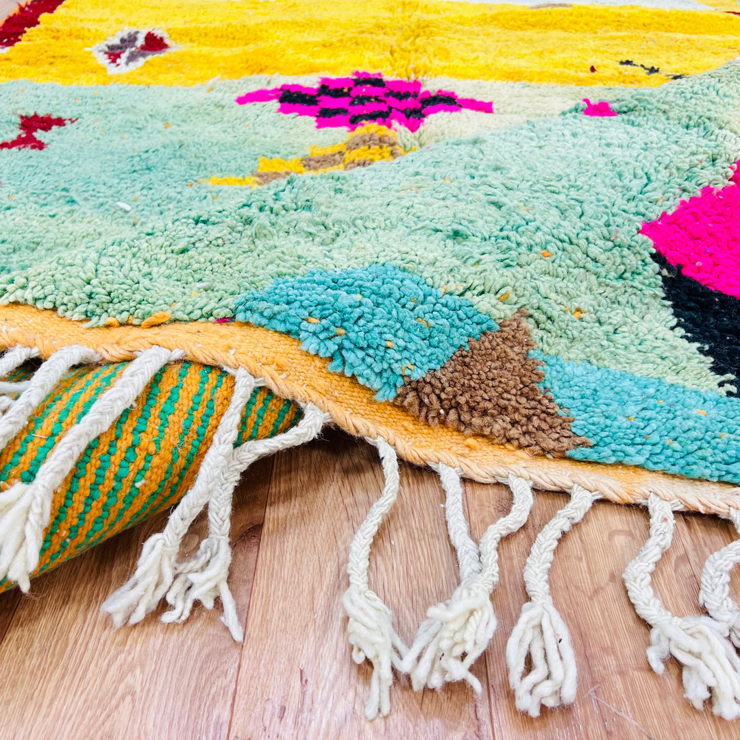 Colorful Berber Moroccan wool rug with tribal patterns and vibrant colors, including pink, green, and yellow, on wooden flooring.