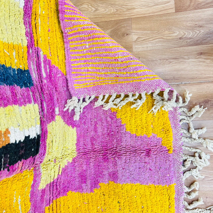 Striped Yellow Moroccan Berber Wool Rug with pink, black, and yellow patterns on a wood floor.
