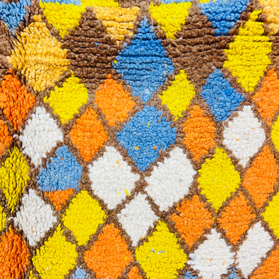 Vibrant diamond patterns on Moroccan wool rug with zigzag design, featuring blue, yellow, orange, and brown hues.