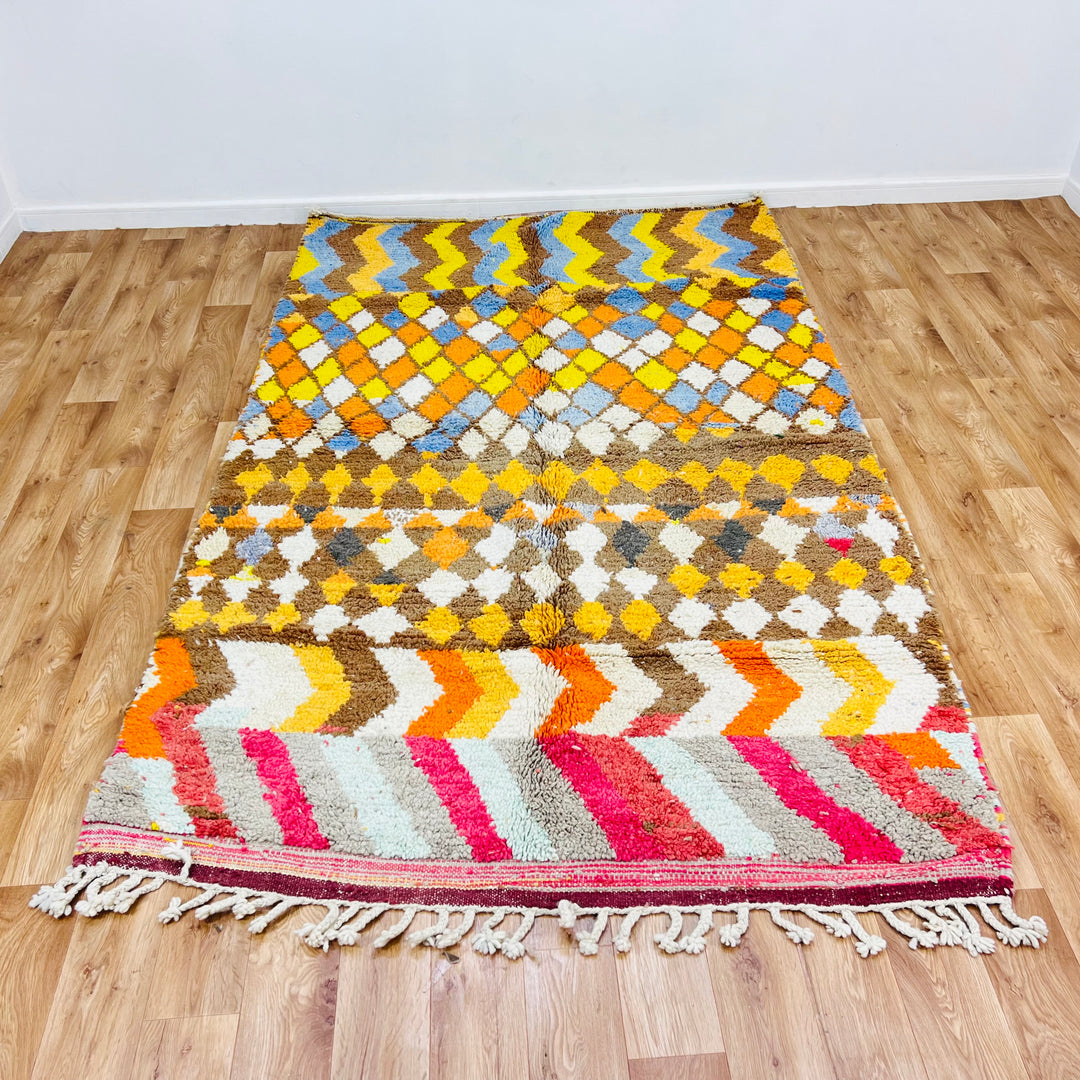 Handmade Moroccan wool rug with geometric zigzag and diamond patterns in vibrant colors on wood floor.