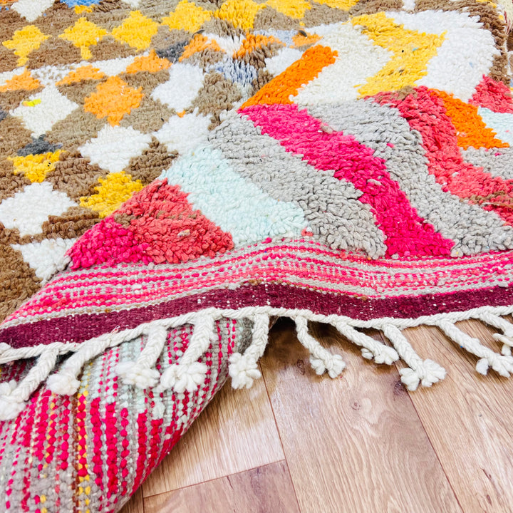 Diamond &amp; Zigzag Moroccan wool rug with vivid pink, orange, and blue patterns, handmade by Berber artisans on wood floor.