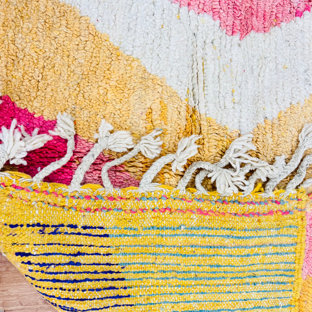 Colorful Moroccan shag rug with vibrant zigzag patterns in pink, mustard, and navy, featuring thick fringed edges.