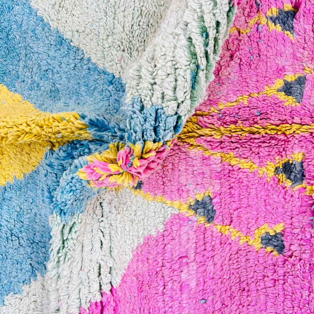 Close-up of vintage Moroccan rug in pink, blue, and yellow with geometric patterns, handwoven in wool by Berber artisans.
