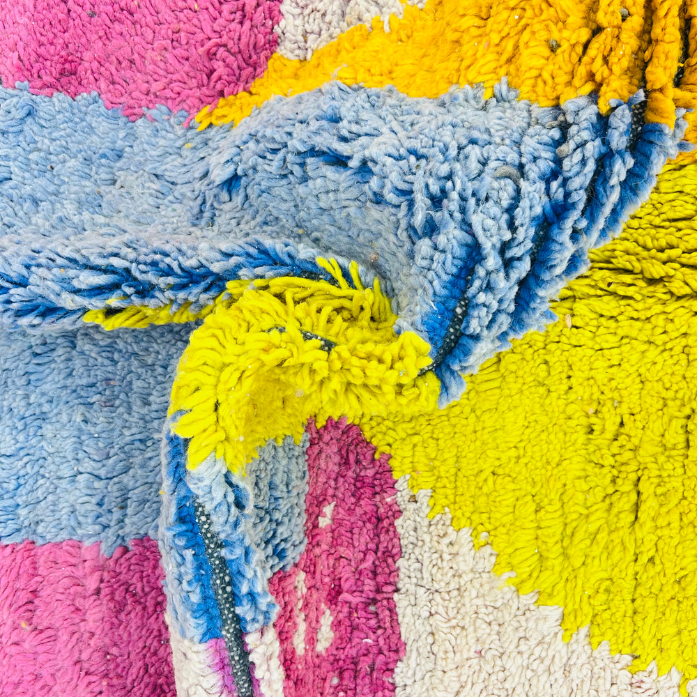 Colorful vintage Moroccan wool rug with pink, blue, yellow abstract design, showcasing Berber geometric symbols and a fluffy texture.
