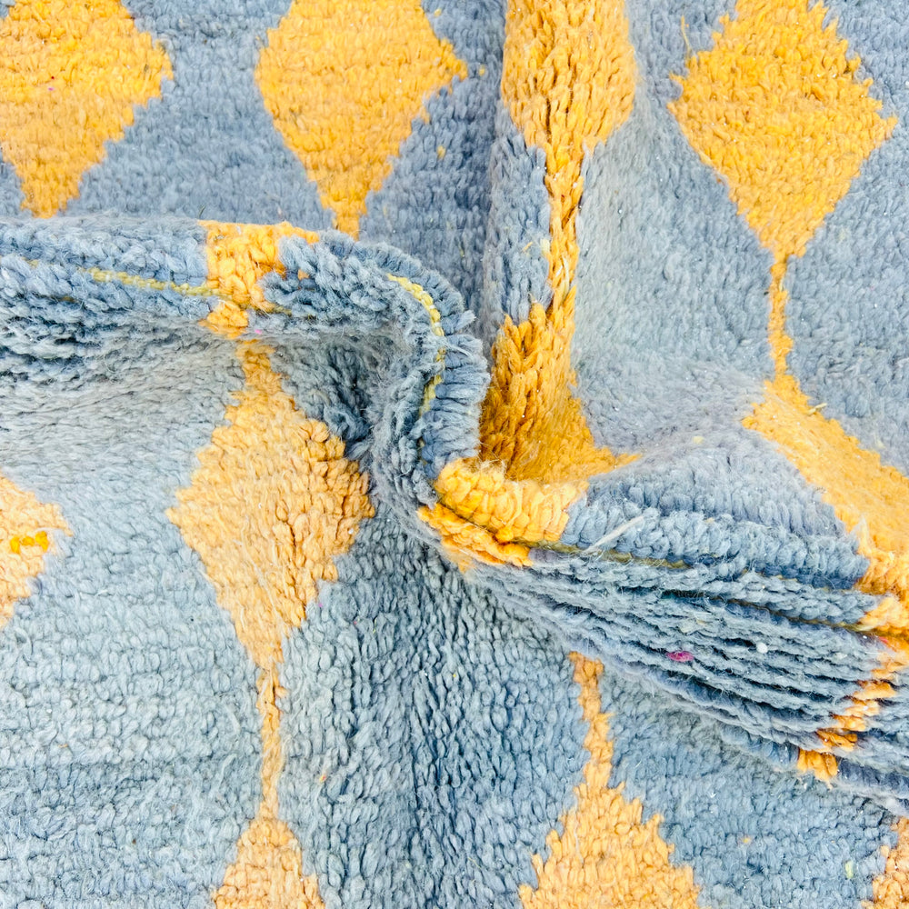 Vintage Moroccan rug with orange and yellow diamond motifs on a grey base, showcasing Berber tradition and geometric design.