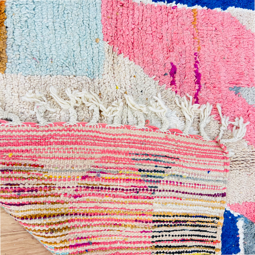 Close-up of a vintage Moroccan rug with pink, beige, blue, and mustard abstract shapes, showcasing handwoven detail.