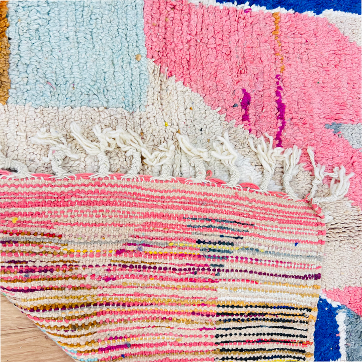 Close-up of a vintage Moroccan rug with pink, beige, blue, and mustard abstract shapes, showcasing handwoven detail.