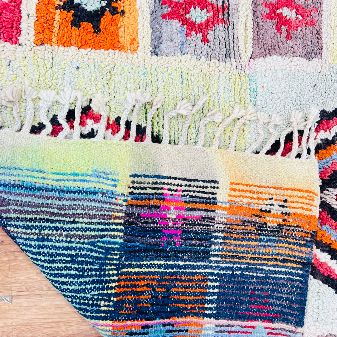 Vintage Moroccan rug with colorful geometric motifs and fringe edges, handmade in soft wool by Berber artisans.