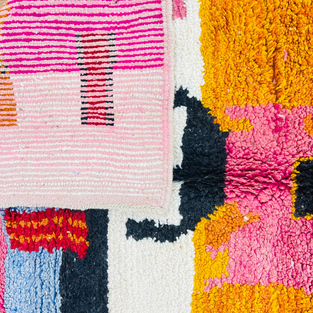 Close-up of vintage Moroccan Berber rug with vibrant red, orange, pink, and blue bands and abstract tribal patterns.