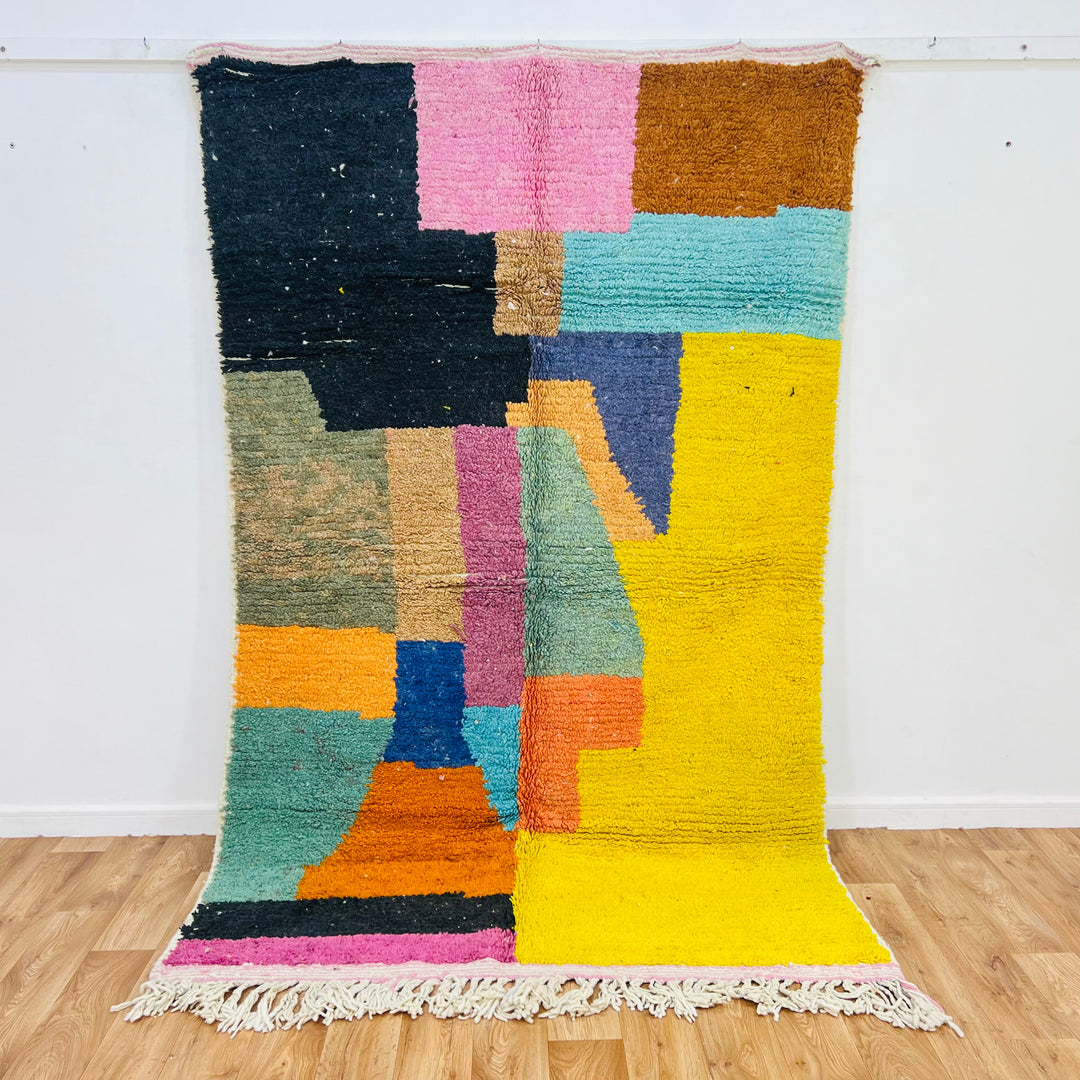 Vintage Moroccan wool rug with abstract color blocks, handmade by Berber artisans. Features yellow, black, pink, and blue patterns.