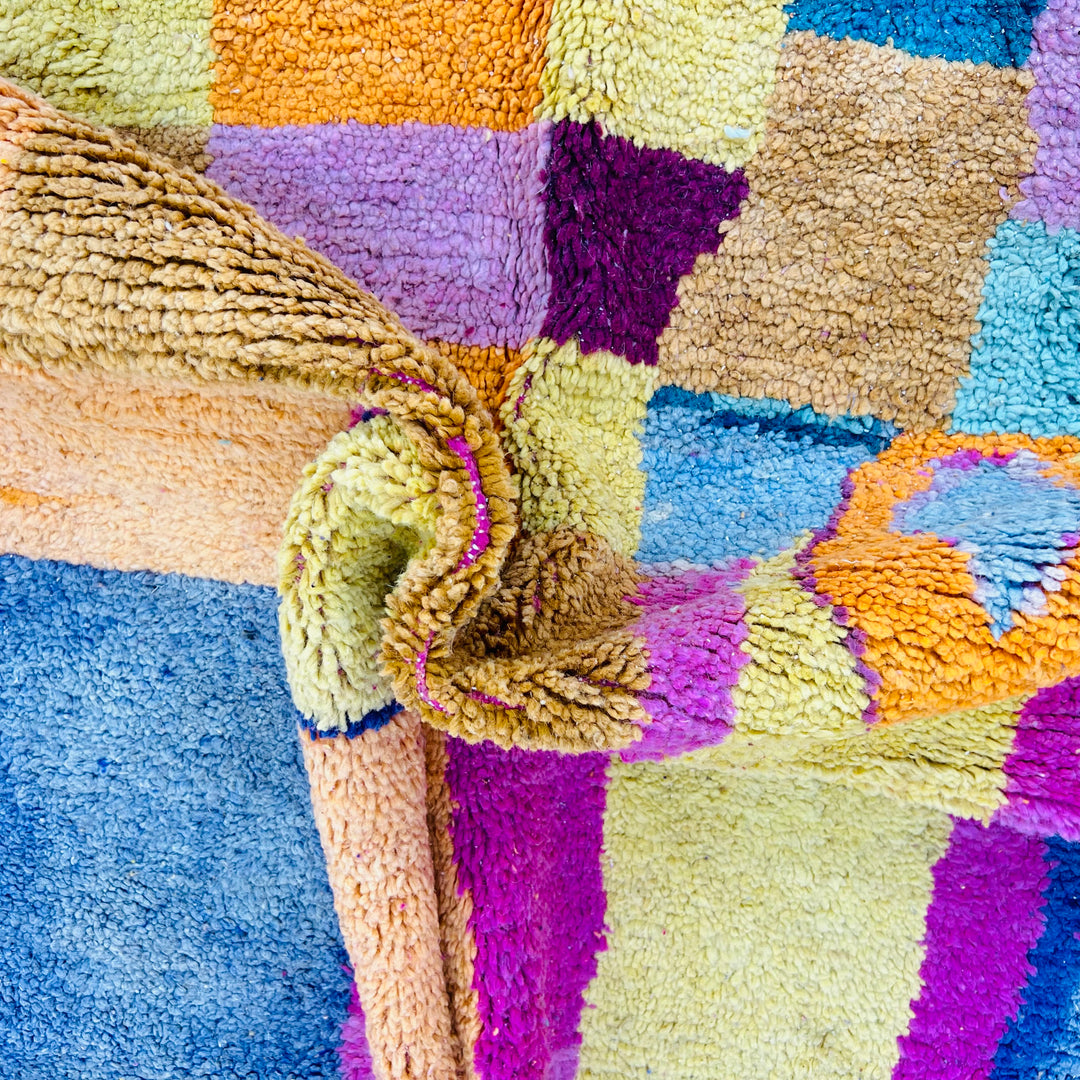 Close-up of vintage multicolor Moroccan rug with vibrant checkered patterns and symbolic diamond accents in wool.