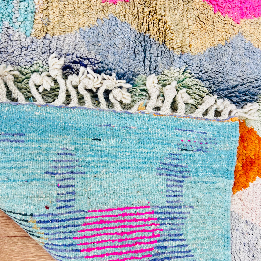 Colorful vintage Moroccan wool rug showing bold diamond pattern in pink, terracotta, and turquoise with a soft blue border.
