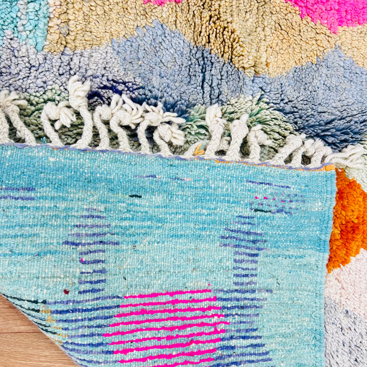 Colorful vintage Moroccan wool rug showing bold diamond pattern in pink, terracotta, and turquoise with a soft blue border.