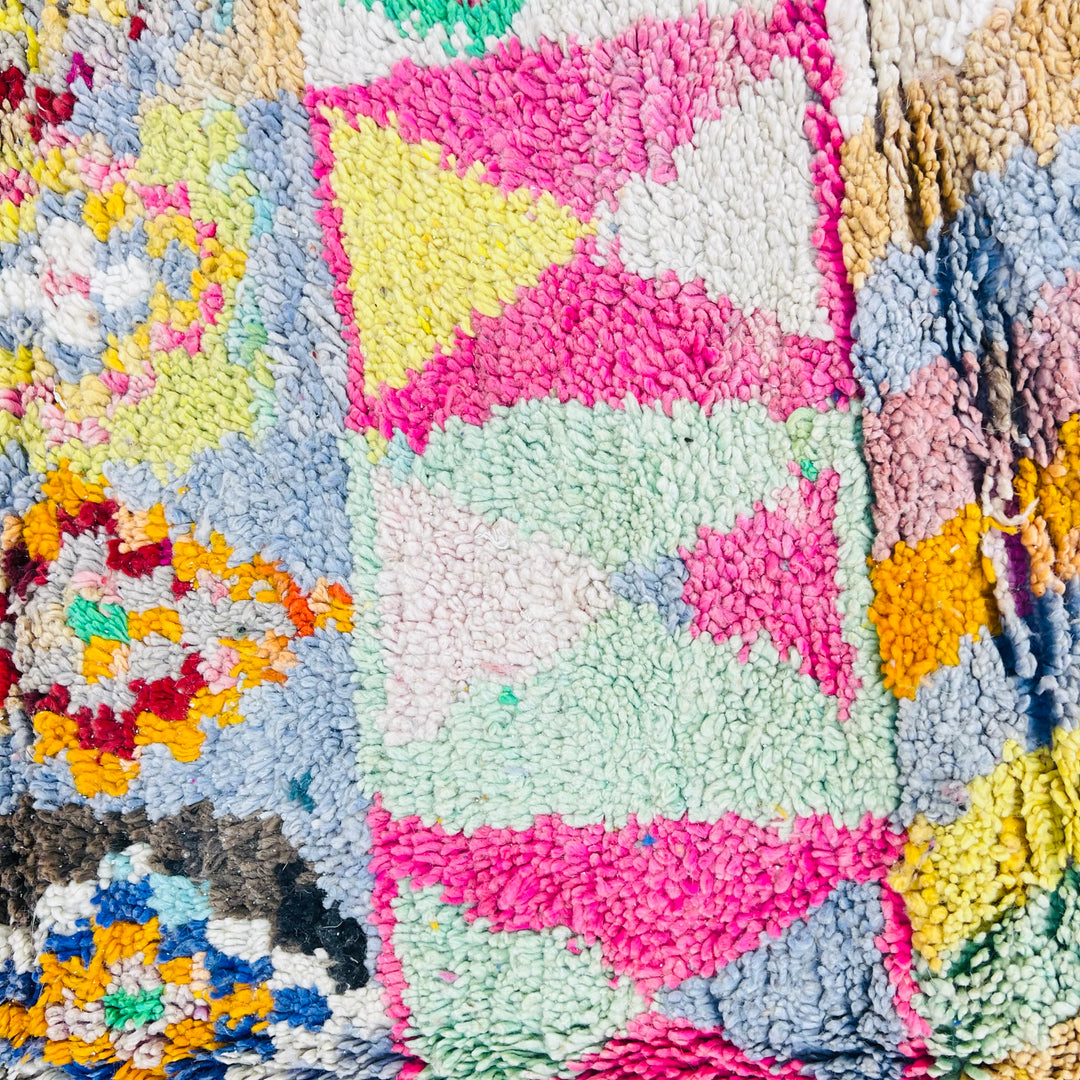 Close-up of a vintage multicolor Berber rug with vibrant tribal motifs and patterns in pink, blue, green, and yellow.