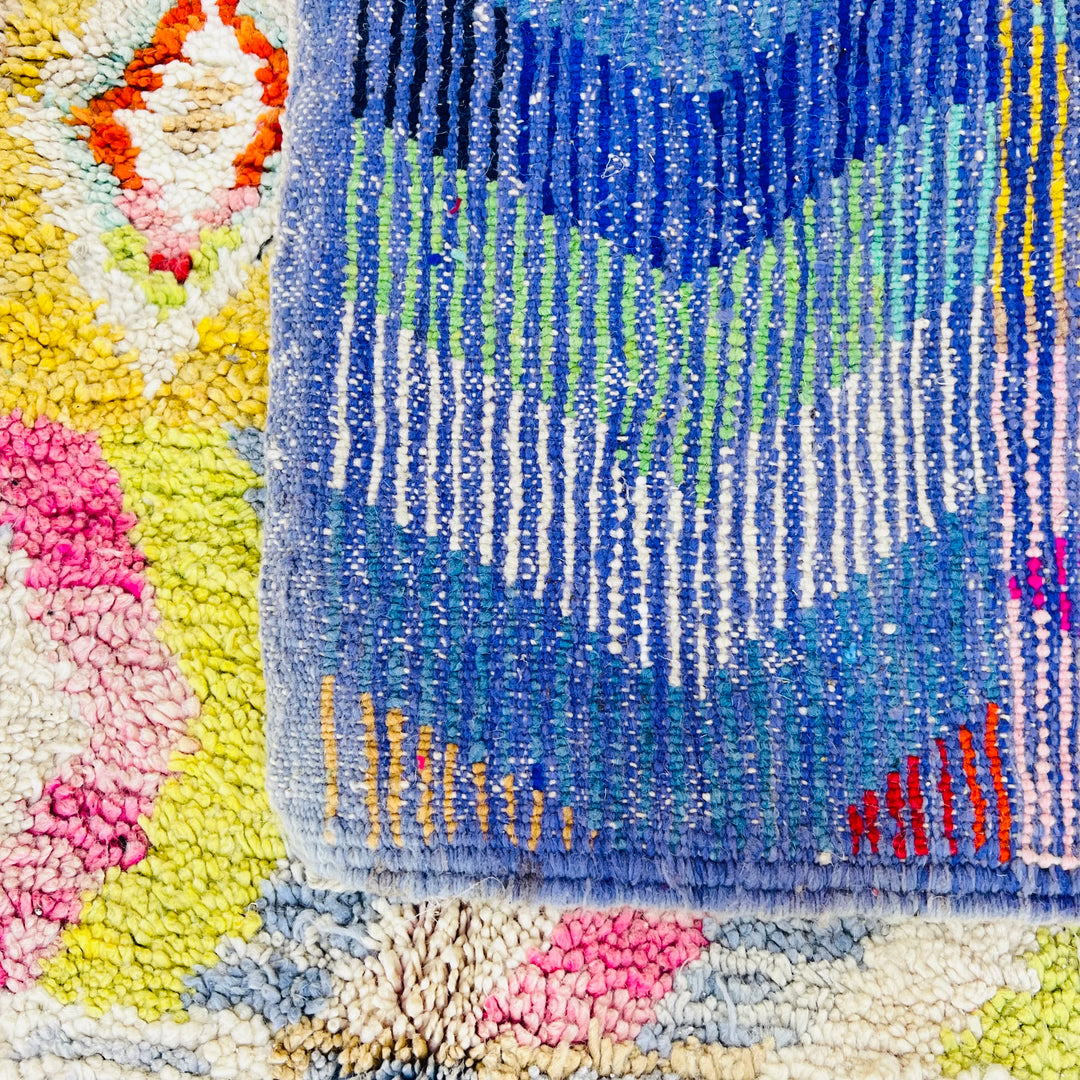 Close-up of a vintage multicolor Moroccan Berber rug with geometric patterns in bright blues, yellows, pinks, and greens.