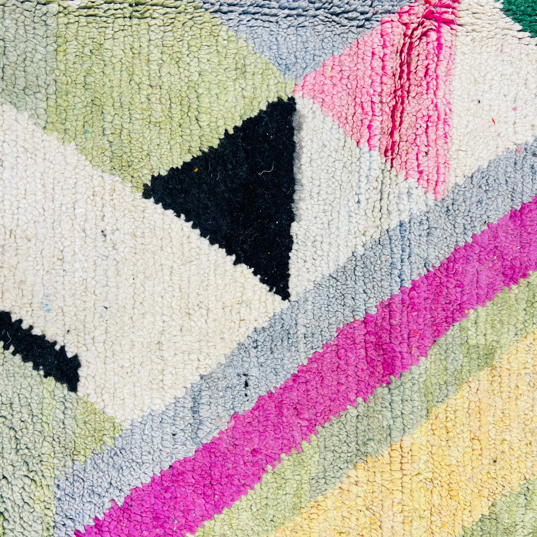Close-up of a vintage Moroccan rug with geometric patterns in pink, green, and black wool, handwoven by Berber artisans.