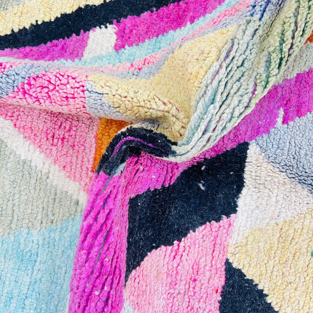 Close-up of a vibrant vintage Moroccan rug with geometric patterns in pink, green, cream, and black. Handmade by Berber artisans from 100% wool.