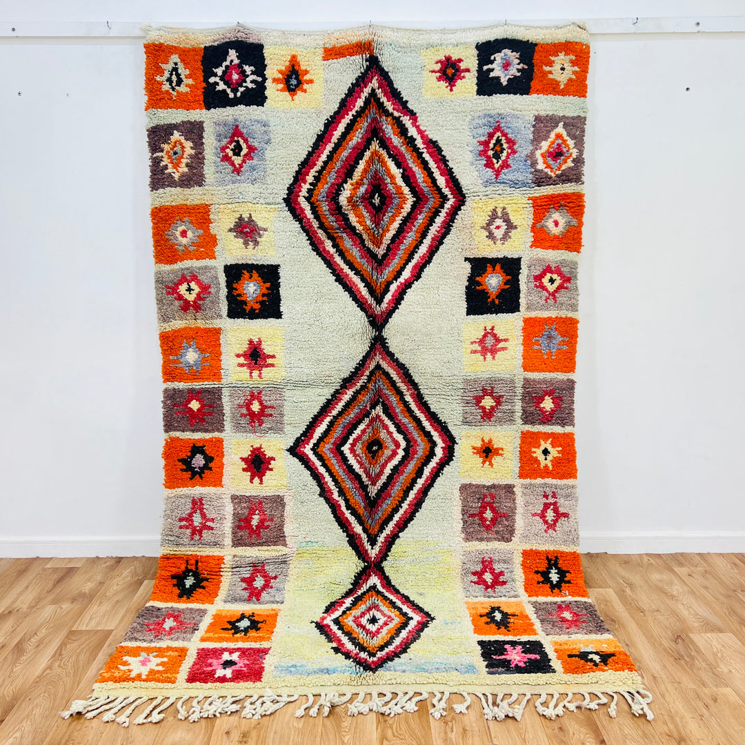 Handmade vintage Moroccan rug with central diamond pattern and geometric star motifs in orange, red, black, and cream. Size: 260 × 155 cm.
