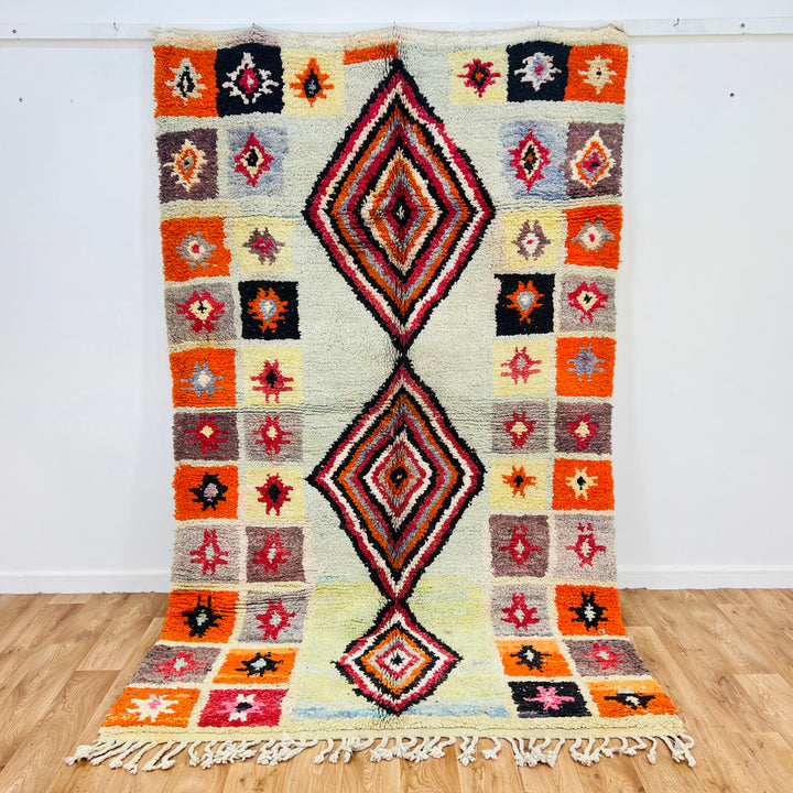 Handmade vintage Moroccan rug with central diamond pattern and geometric star motifs in orange, red, black, and cream. Size: 260 × 155 cm.