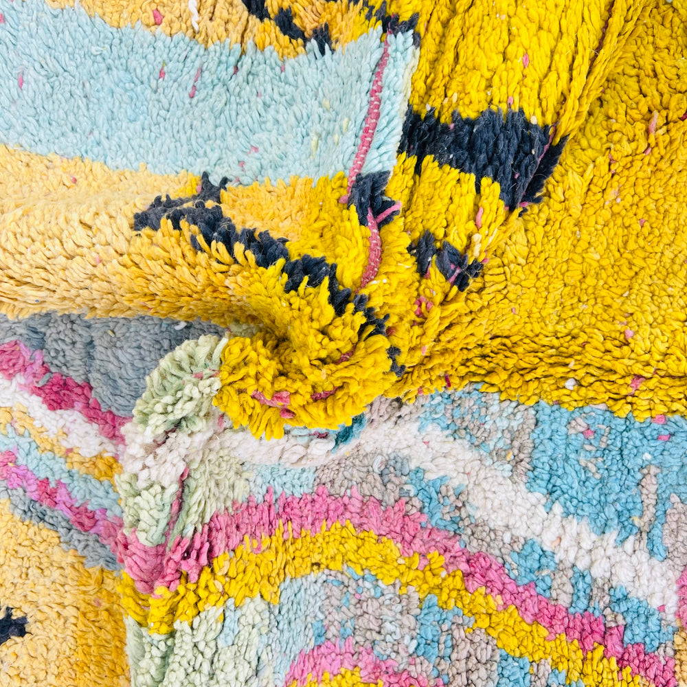 Close-up of a colorful vintage Moroccan rug showcasing abstract patterns and bold colors like yellow, blue, and pink. Handwoven wool texture.