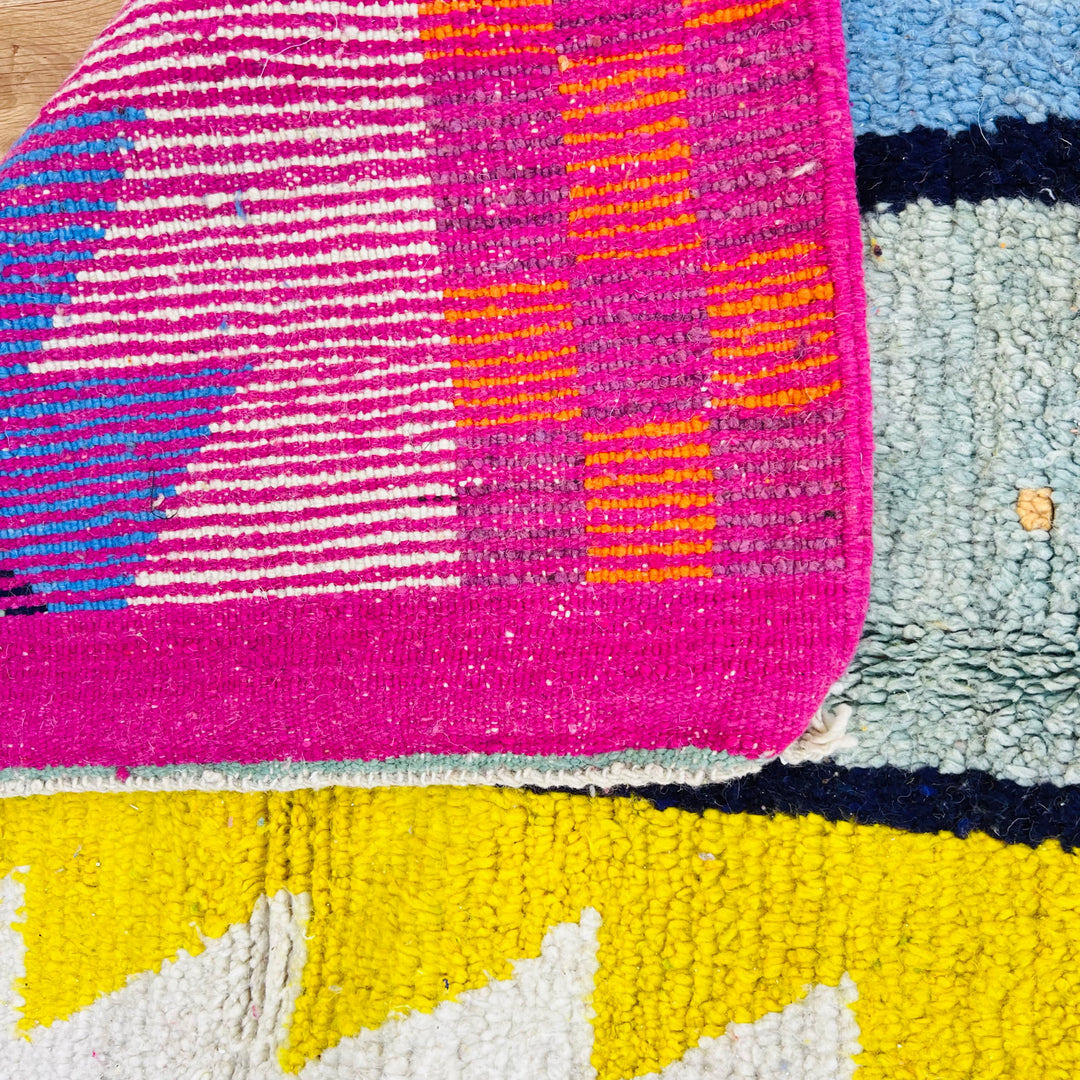 Close-up of a colorful vintage Moroccan rug with magenta, yellow, and blue abstract patterns, handwoven with premium wool.