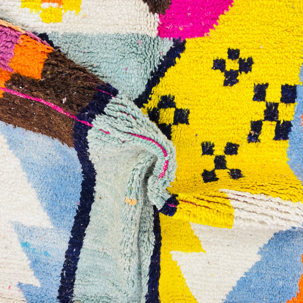 Close-up of colorful vintage Moroccan rug with abstract Berber patterns, showcasing vibrant magenta, yellow, and blue motifs.