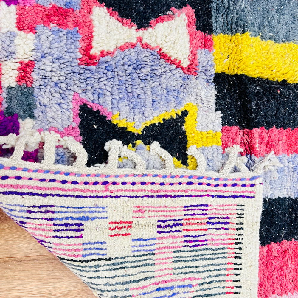 Vintage Moroccan rug with vibrant geometric patterns in pink, yellow, blue, and black. Hand-knotted Berber artistry showcased.