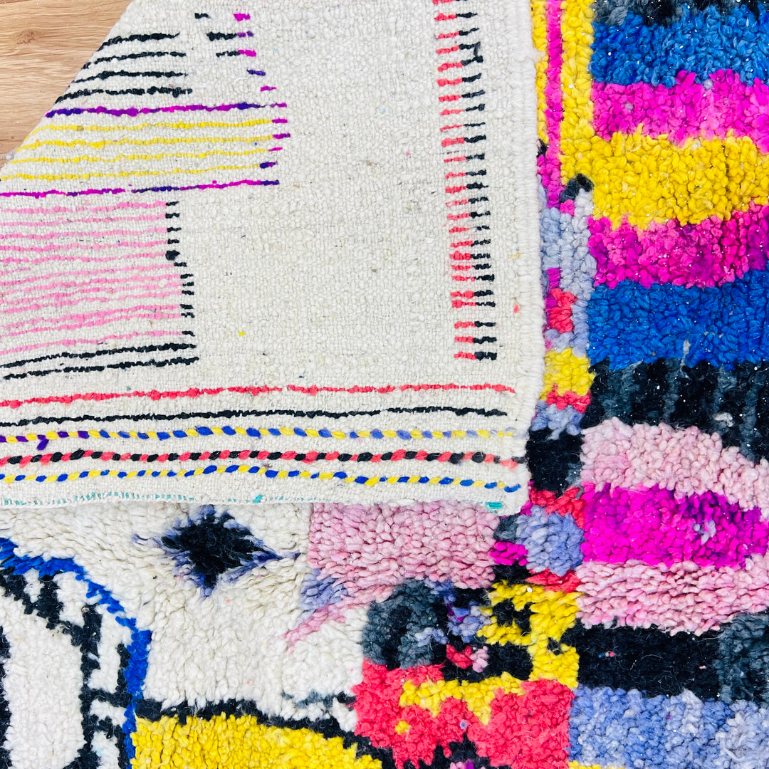 Close-up of a vibrant vintage Moroccan rug with geometric patterns in pink, yellow, blue, and black, showcasing Berber artistry.